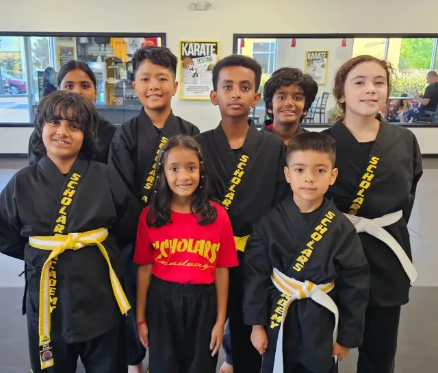 Group of children in martial arts uniforms and sashes posing together indoors, smiling at the camera